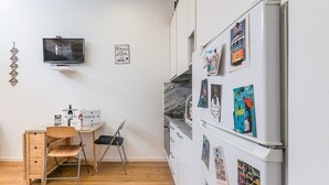 Une cuisine compacte avec un réfrigérateur décoré d’aimants sur le thème du voyage, un bureau en bois avec une chaise et un téléviseur fixé au mur.