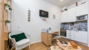 Une cuisine moderne avec des meubles blancs, un four à micro-ondes et un évier. On y trouve une table à manger en bois avec des chaises, et un téléviseur fixé au mur.