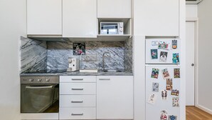 Une cuisine compacte avec des meubles blancs, un four à micro-ondes encastré, un four en acier inoxydable et un réfrigérateur décoré de photos d’enfants.