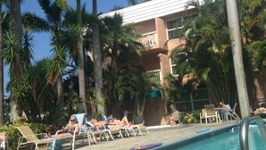A pool area with lounge chairs and palm trees, surrounded by a building with a white roof and beige walls. - 5 min walk to beach on inter coastal waterway (Fort Lauderdale)