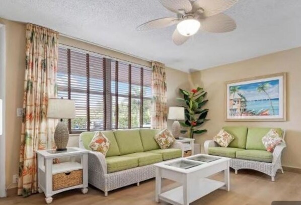 Un salon avec un canapé vert, une table basse blanche et un ventilateur de plafond.
