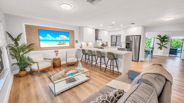 A modern living room with a glass coffee table, a sofa, and a kitchen area with a bar. - Chic + Upscale + Heated Pool | 15 min FLL & Beach (Plantation)
