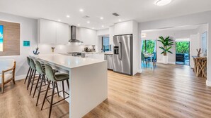 A modern kitchen with a large island, stainless steel appliances, and a view to a dining area. - Chic + Upscale + Heated Pool | 15 min FLL & Beach (Plantation)