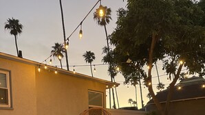 Un patio al aire libre con mobiliario de mimbre, una chimenea y luces colgantes.