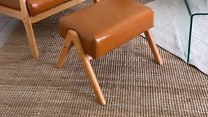 Un salón con un sillón de cuero, un banco de madera, un sofá gris con cojines, una lámpara de pie y un cuadro en la pared.