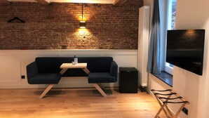 Un salon chaleureux avec un mur en briques, un plafond en bois, un téléviseur noir, un canapé bleu, une petite table et une fenêtre avec des rideaux.