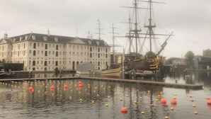 Un bâtiment historique, avec un grand plan d’eau devant, et un grand voilier amarré à proximité.