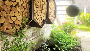 Une présentation de bûches de bois hexagonales, fixée sur un mur de briques, entourée de verdure et d’une plante en pot.