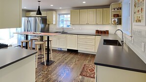 A modern kitchen with a central island, wooden flooring, and white cabinetry. - Compound for Families- Main House with Adjacent Cottages Cabins,Indoor Pool Spa (Fennville)