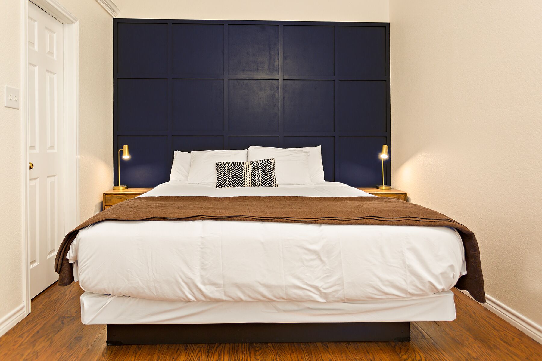 A neatly made bed with white linens and a brown throw blanket, a dark headboard, and two bedside lamps on wooden nightstands.