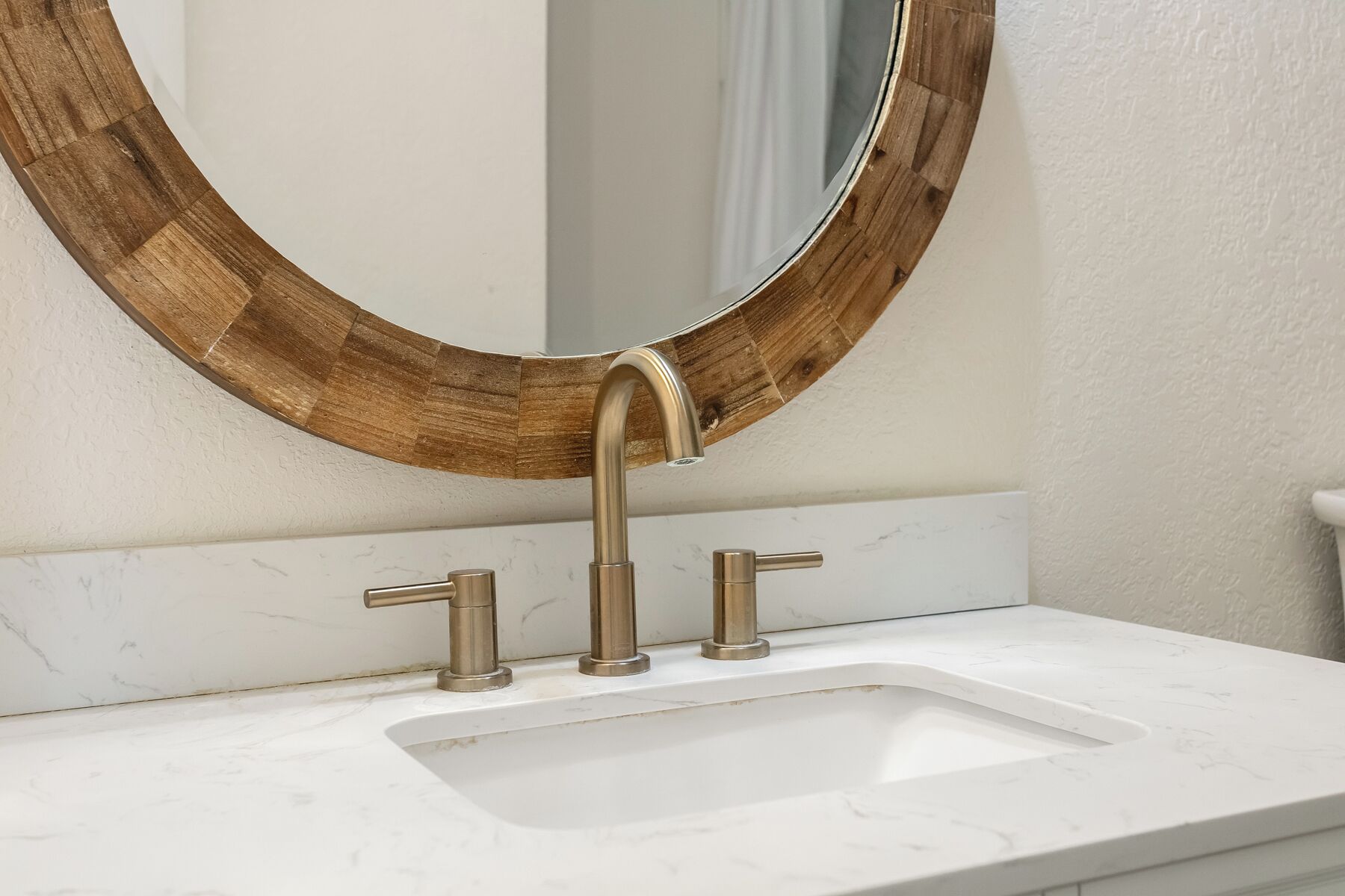 Une salle de bain avec un lavabo en marbre blanc, un miroir encadré en bois et un robinet moderne.
