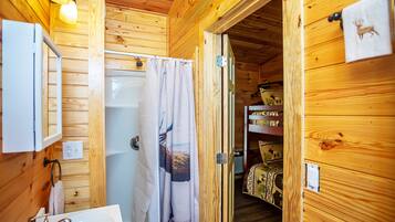 Baño de cabaña de madera con lavabo, espejo y cortina de ducha.