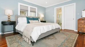 A bedroom with a bed, two bedside tables, a dresser, and a door leading to another room.