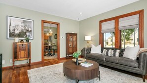 A living room with a dark leather sofa, a round wooden coffee table, and a large window with blinds.