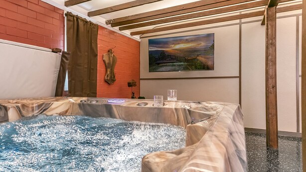 A room with a hot tub, a painting on the wall, and a brick wall.