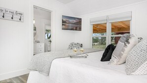 Una camera da letto con un letto, un comodino con due bicchieri di vino, un quadro appeso al muro e una finestra vista all'esterno.