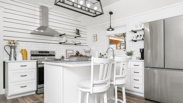 Una cucina moderna con mobili bianchi, un frigorifero in acciaio inossidabile e un'isola centrale con sgabelli da bar.