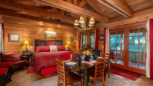 Interior acogedor de una cabaña de troncos con una cama de madera, una mesa de comedor con sillas y una araña.