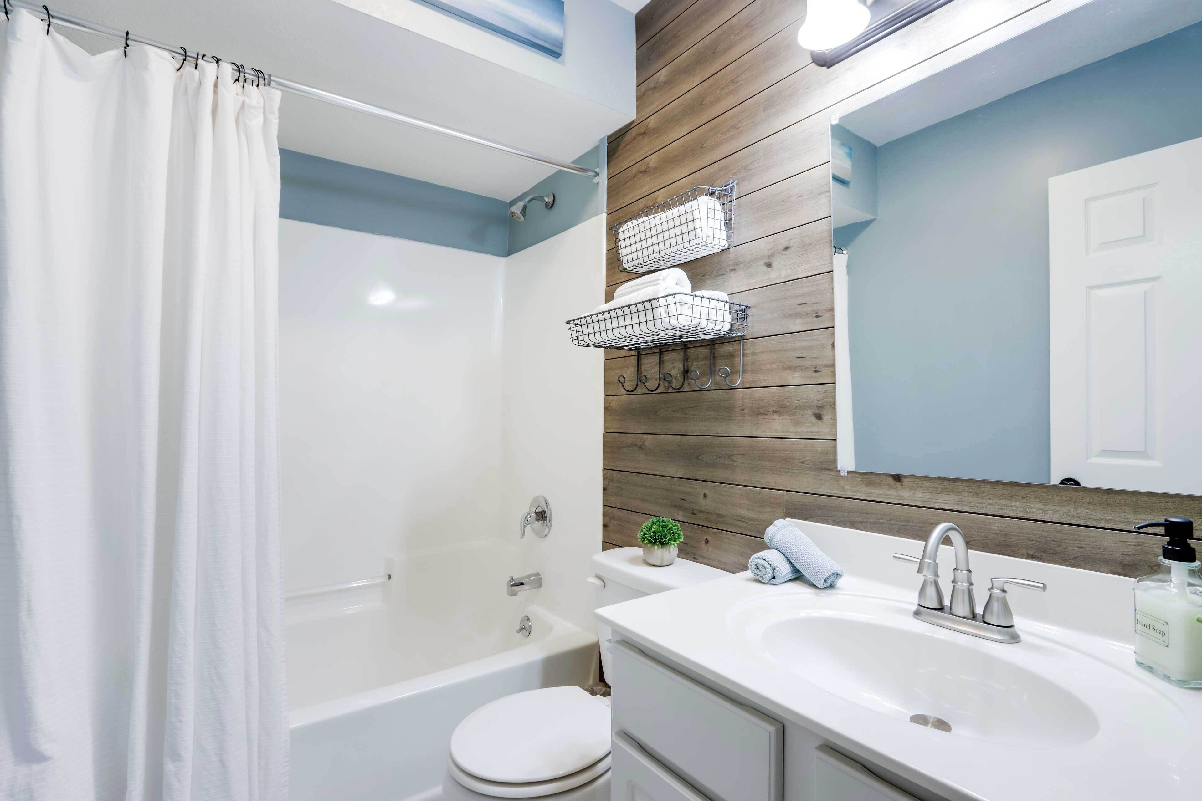 Un bagno moderno con tenda da doccia, vasca, servizi igienici, lavandino con specchio e rivestimento in legno.