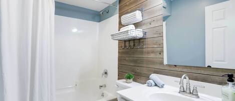 Un bagno moderno con tenda da doccia, vasca, servizi igienici, lavandino con specchio e rivestimento in legno.