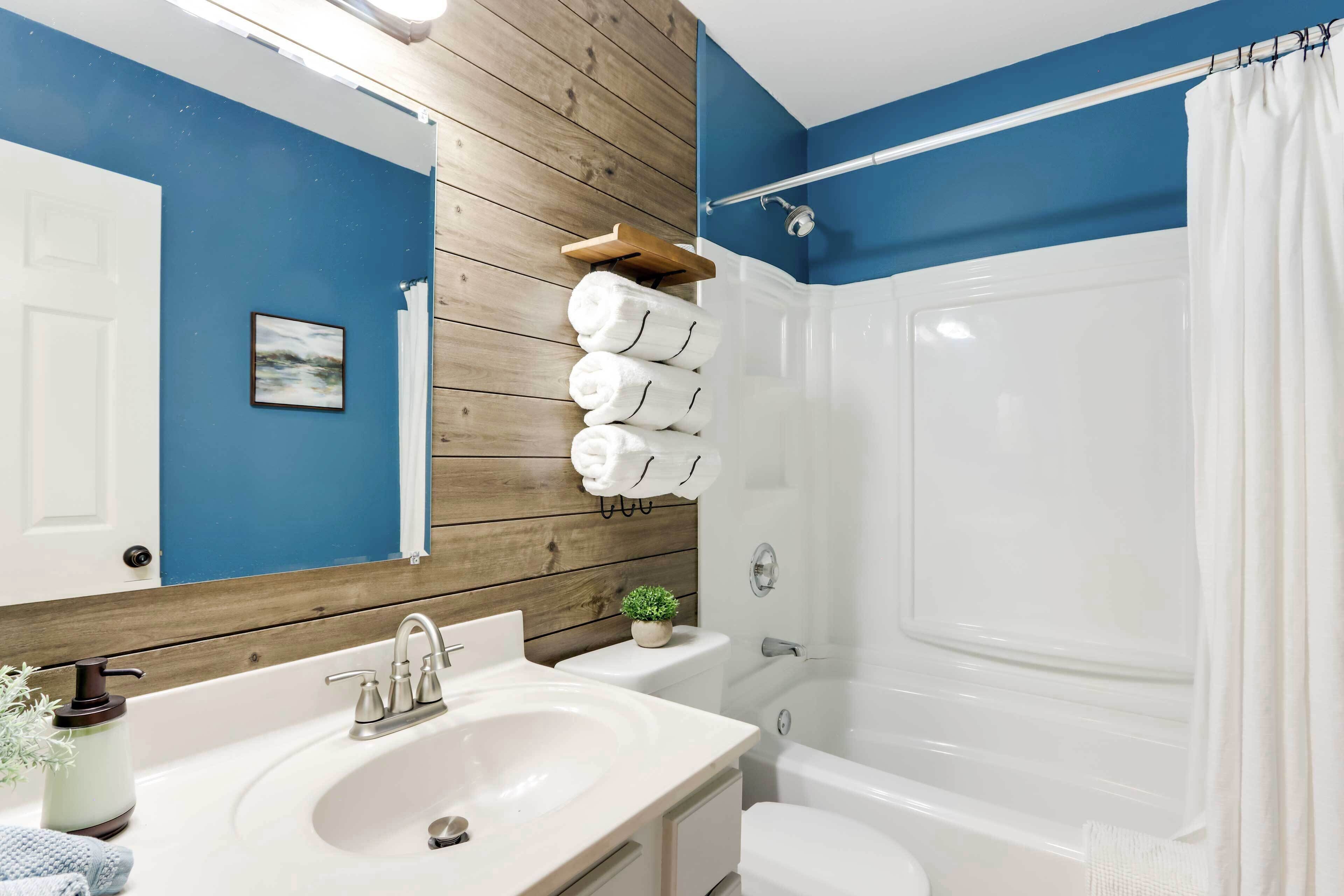Un baño con pared de madera, pared de acento azul, lavamanos blanco, inodoro y ducha con cortina.