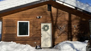 Eine Holzjagdhuette mit schneebedecktem Dach, einer Eingangstür, einem Fenster und einem Kranz an der Tür.