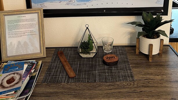 Eine Weltkarte an der Wand, ein gerahmter Zettel, ein kleiner Blumentopf, ein Glas mit dekorativen Steinen und ein hölzernes Objekt auf einem Tisch.