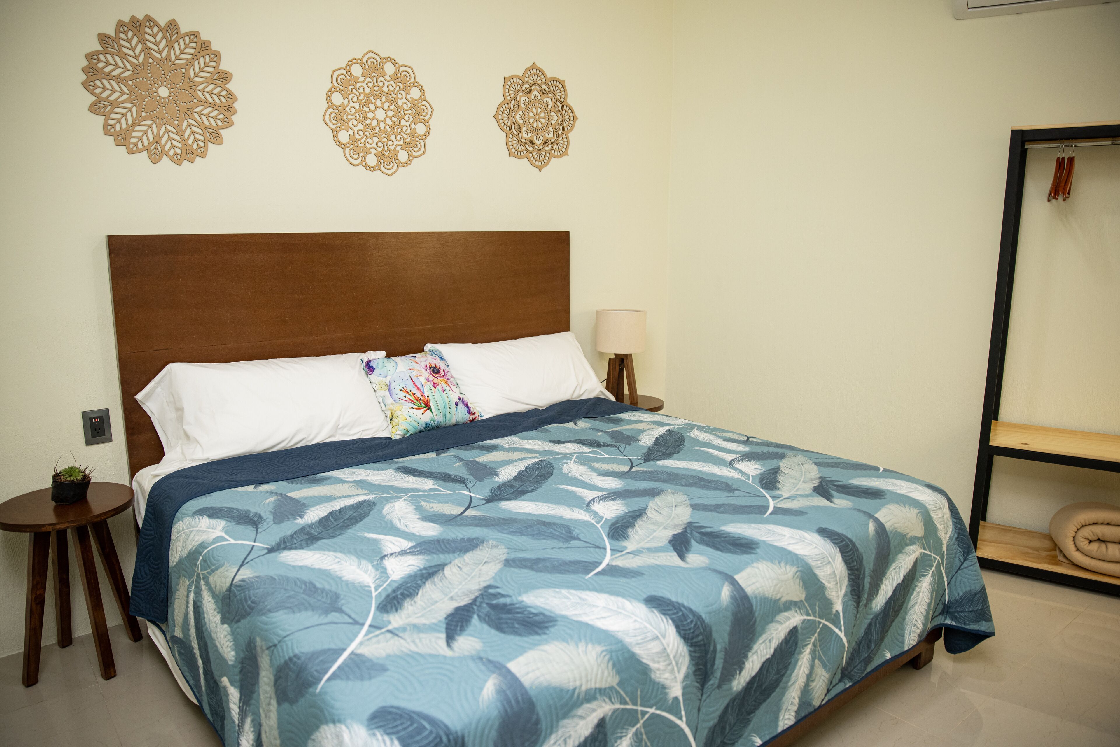 A neatly made bed with a blue and white feather pattern bedspread, a wooden headboard, and decorative wall art above it.