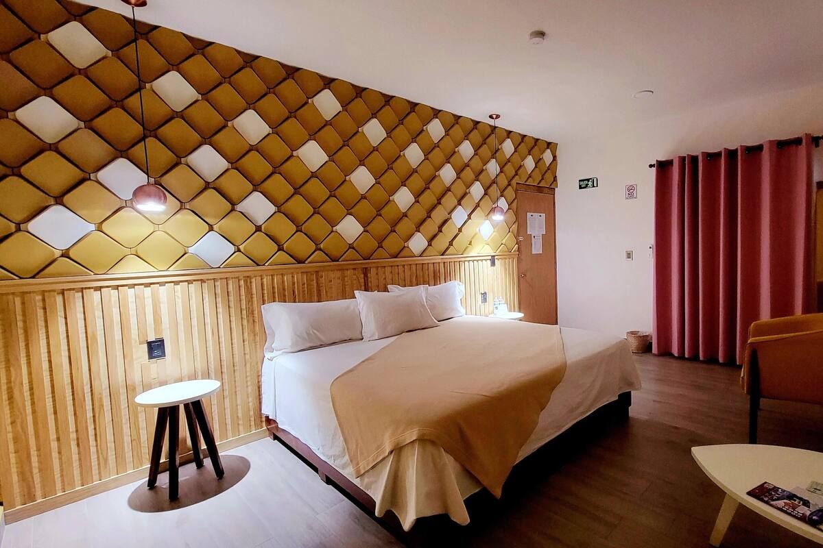 A hotel room with a bed, a small table, a chair, and a decorative wall.
