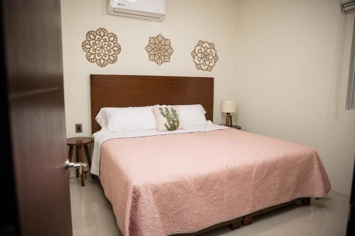 A neatly made bed with a pink bedspread, a wooden headboard, and decorative wall art.