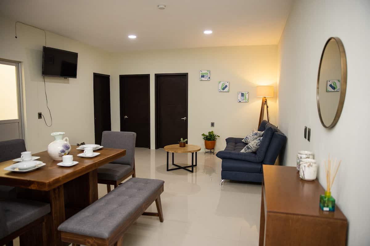 A modern living room with a dining area, a sofa, a coffee table, and a TV mounted on the wall.