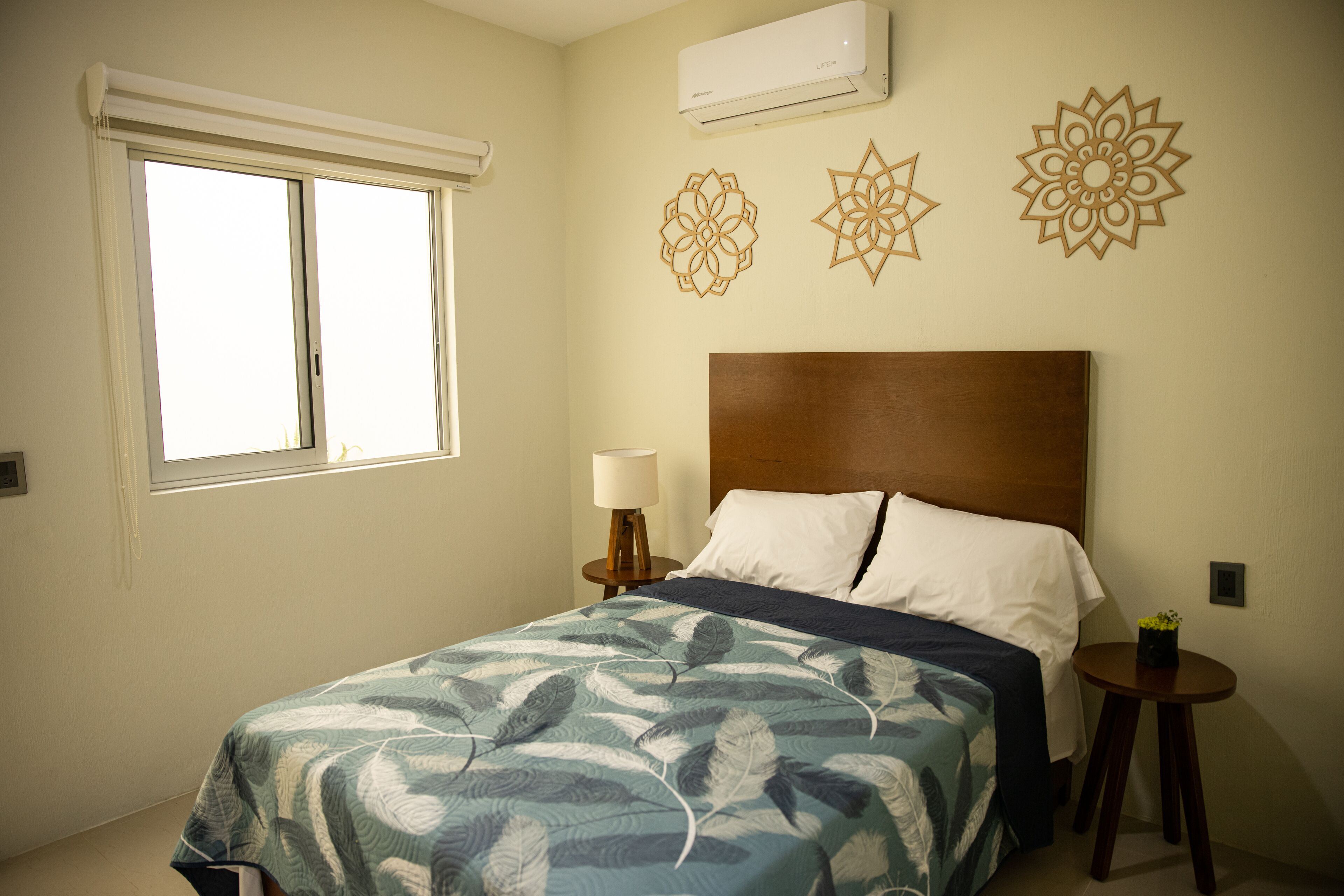 A bedroom with a bed, a window, a nightstand, and decorative wall art.