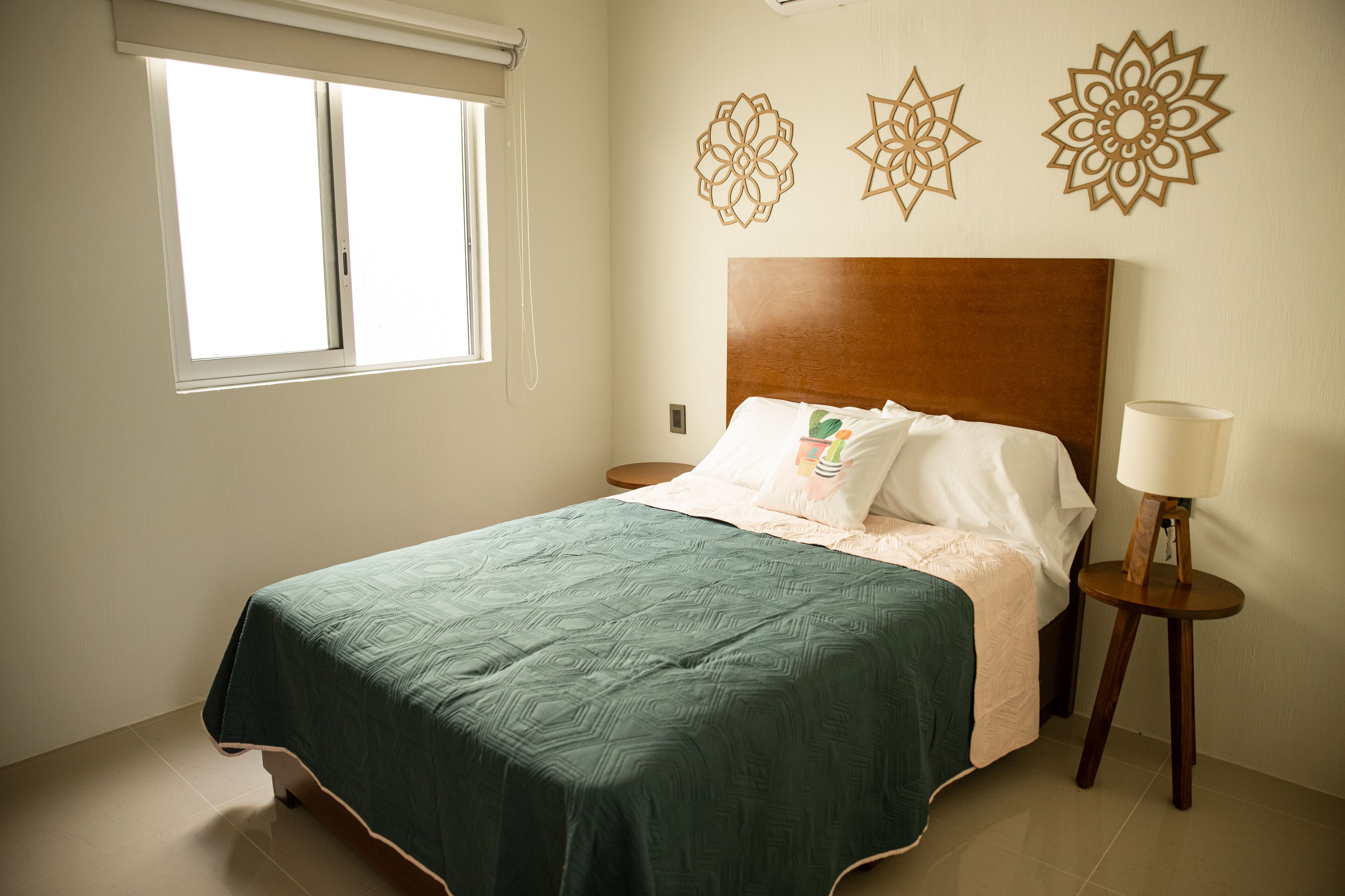 Una cama bien hecha con edredón verde, cabecera de madera y decoración mural.