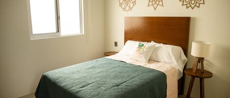 Una cama bien hecha con edredón verde, cabecera de madera y decoración mural.