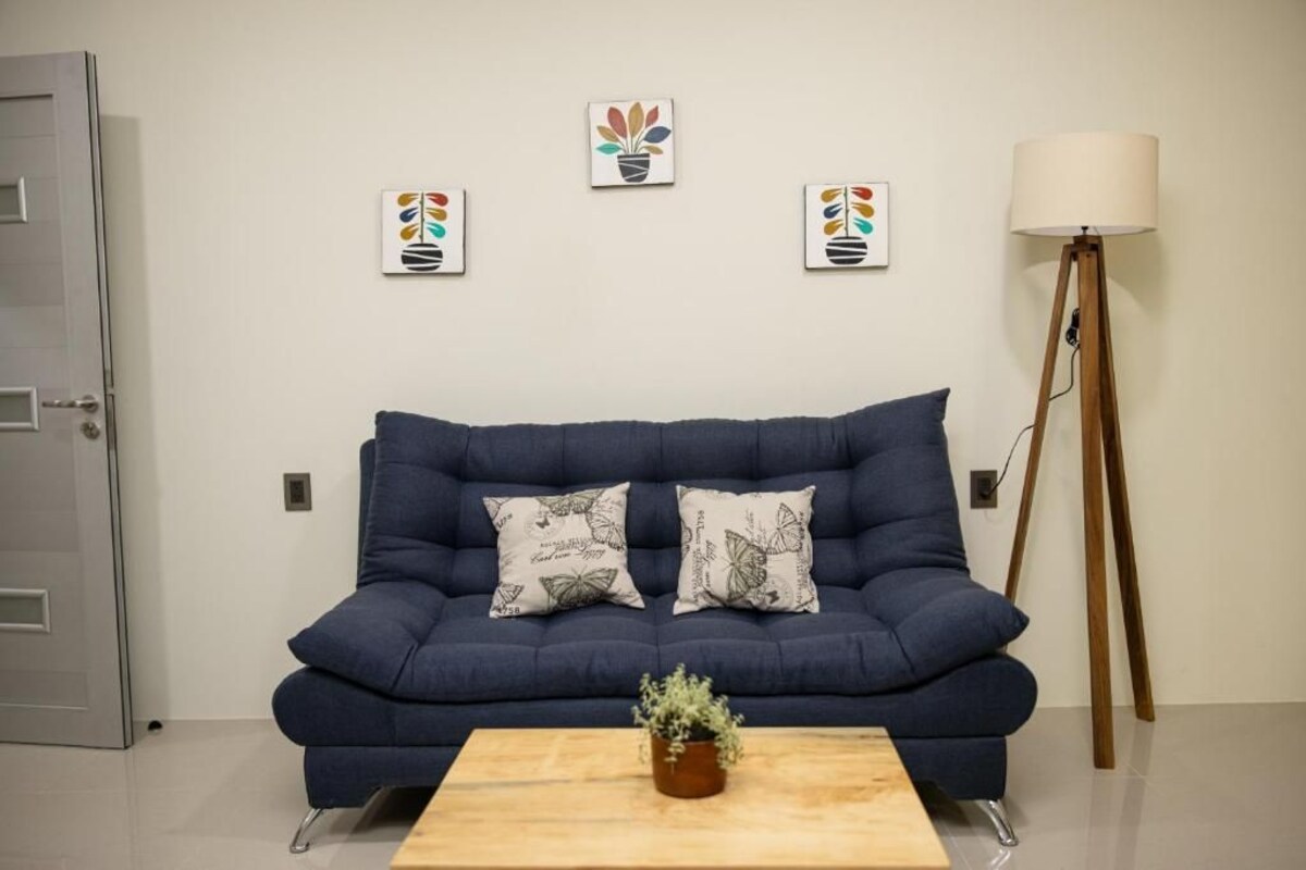 A blue sofa with butterfly-patterned pillows, a wooden coffee table with a plant, and a floor lamp.
