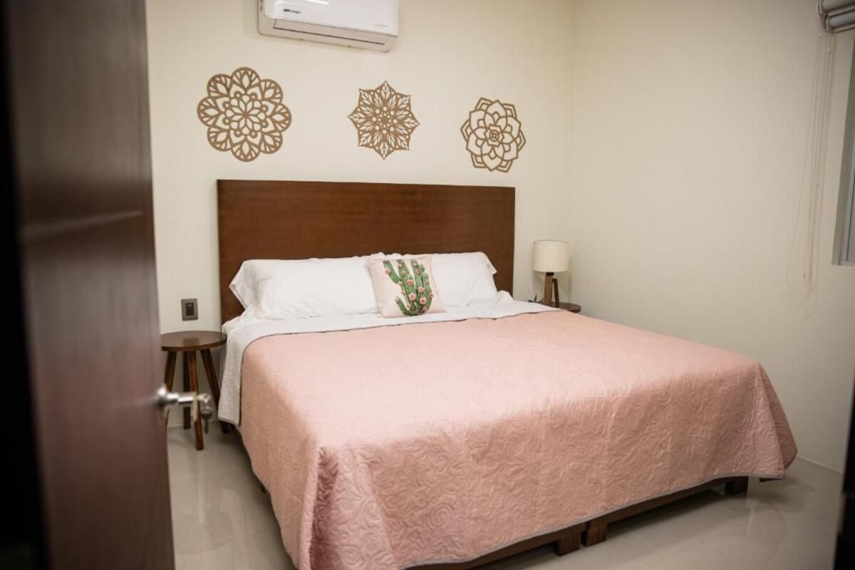 A neatly made bed with a pink bedspread, a wooden headboard, and decorative wall art.