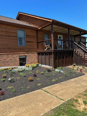 Een houten gebouw met een overdekte veranda, een gevel van baksteen en een aangelegde tuin met diverse planten.