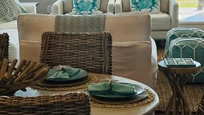 A living room with a view of the ocean, a ceiling fan, and a dining area with wicker furniture. - STUNNING BEACHFRONT WITH TRIPLE WATER VIEWS OF OCEAN, LAKE, BAY! (Galveston)