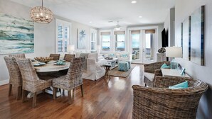 A spacious living area with a dining table, wicker chairs, and a ceiling fan. - STUNNING BEACHFRONT WITH TRIPLE WATER VIEWS OF OCEAN, LAKE, BAY! (Galveston)