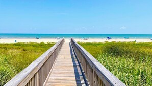 A wooden boardwalk leading to a beach with clear skies and calm waters. - STUNNING BEACHFRONT WITH TRIPLE WATER VIEWS OF OCEAN, LAKE, BAY! (Galveston)