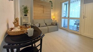 Una sala moderna con un sofá, una mesa de comedor con sillas, una lámpara y un ventanal con vistas al exterior.