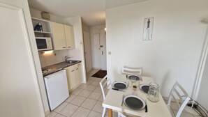 A compact kitchen with white cabinets, a microwave, and a sink. There is a dining area with a table set for two, chairs, and a small potted plant. - Royan - APARTMENT with SEA VIEW - ONLY 300m from the BEACH and SHOPS (ROYAN)