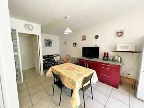 A compact kitchen with a dining table, chairs, a TV, a microwave, and a coffee maker.
