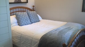 A neatly made bed with patterned pillows, a wall-mounted light, and a framed deer picture. - Cozy Studio (Sandpoint)
