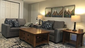 A living room with a grey sofa, patterned cushions, a wooden coffee table, two side tables with lamps, and a large rug. - Cozy Studio (Sandpoint)