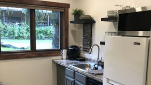 A compact kitchen with a built-in dishwasher, a stainless steel refrigerator, and a window overlooking a backyard. - Cozy Studio (Sandpoint)