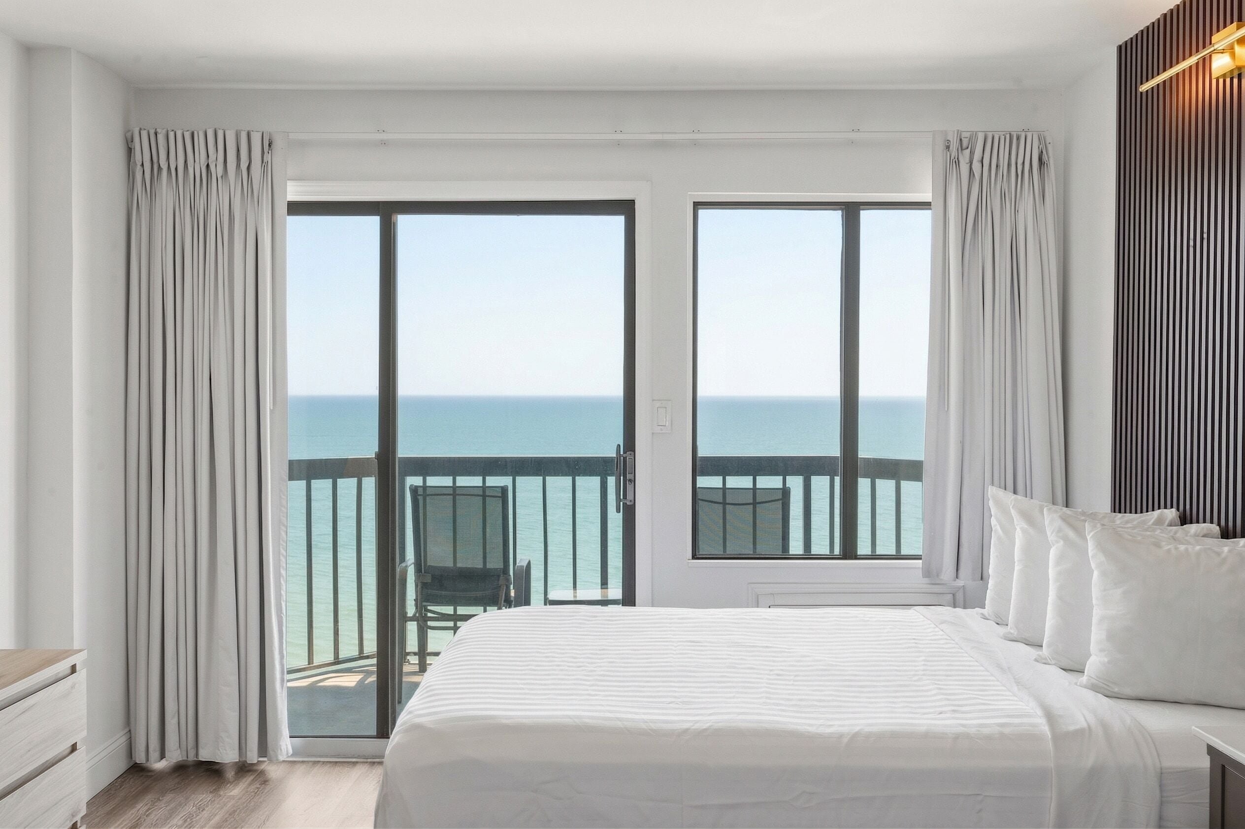 Een hotelkamer met een groot bed, een balkon met uitzicht op zee en een houten hoofdeinde.