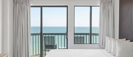 Een hotelkamer met een groot bed, een balkon met uitzicht op zee en een houten hoofdeinde.
