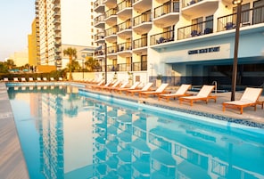 Una piscina con sillas de descanso, un edificio de hotel y un letrero que dice 'GRAND BEACH RESORT'.