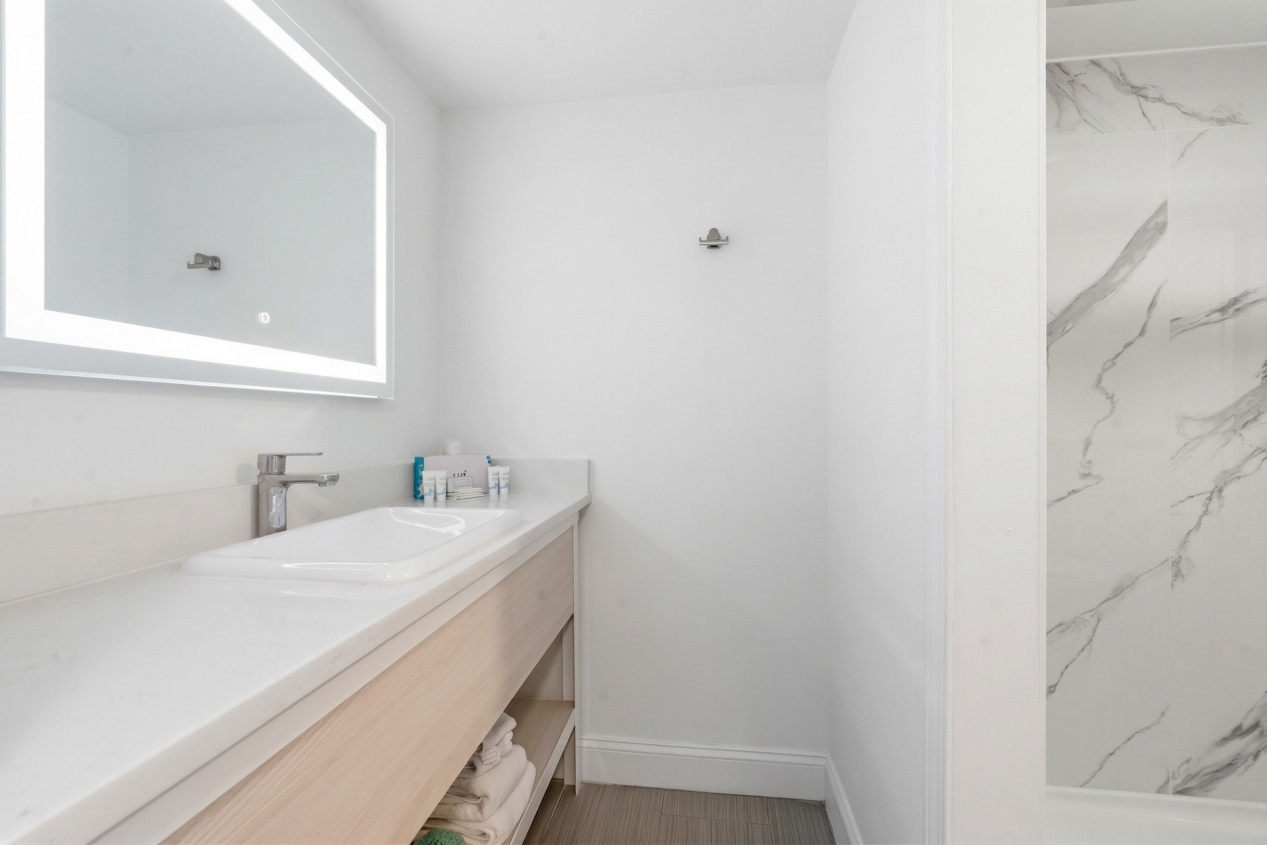A bathroom with a white sink, mirror, and marble shower.